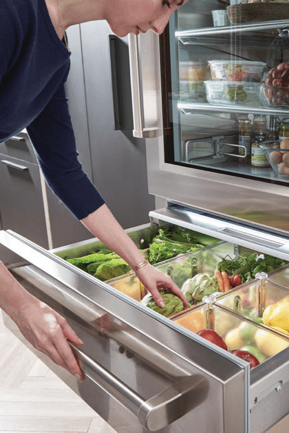 Woman putting fresh vegetables in luxury refrigerator