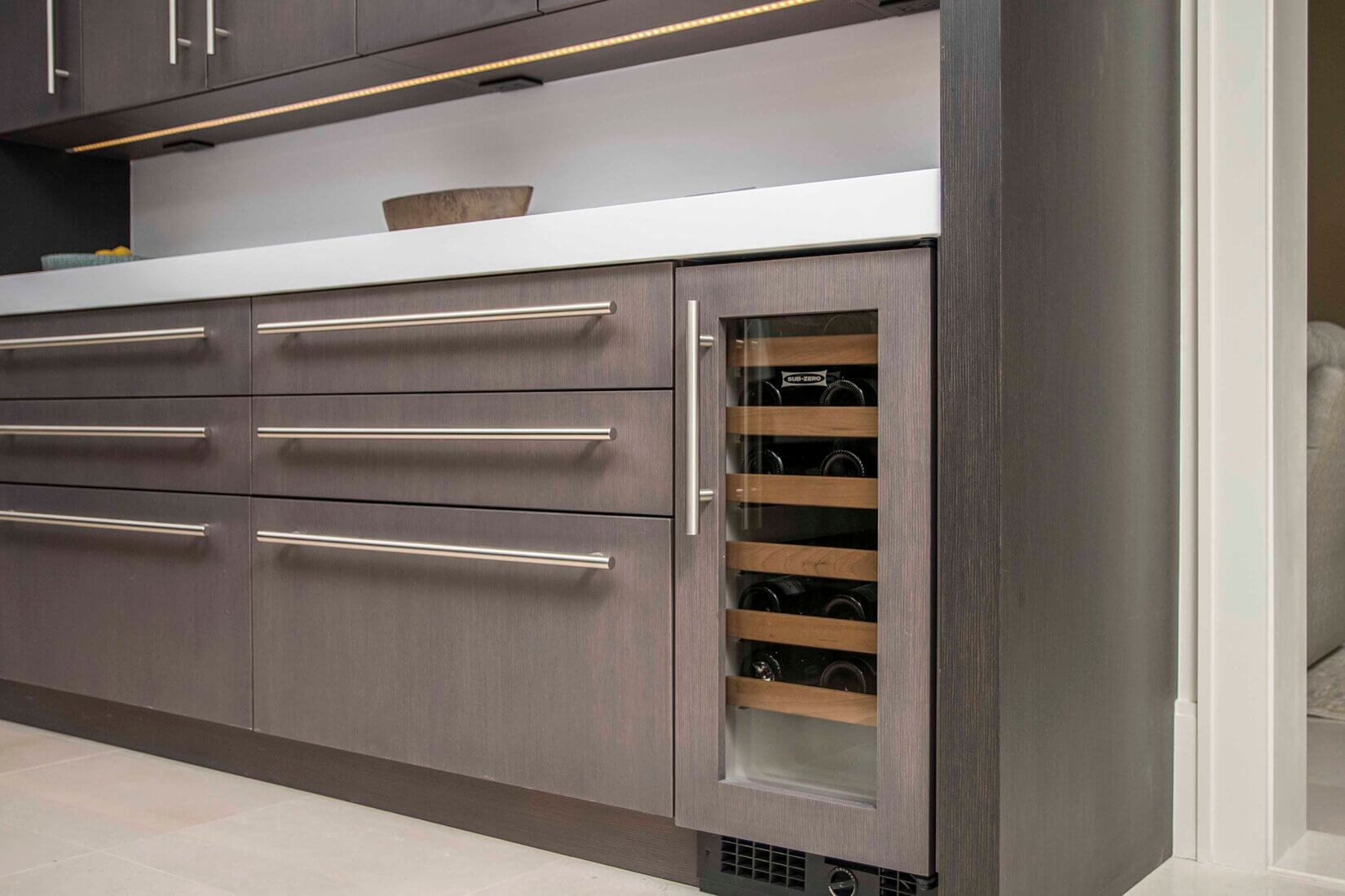 Small wine cooler built into luxury gray-wood cabinetry